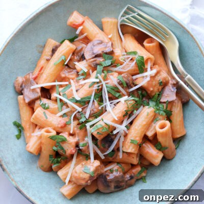 creamy tomato chicken and mushroom pasta in blue bowl with gold silverware