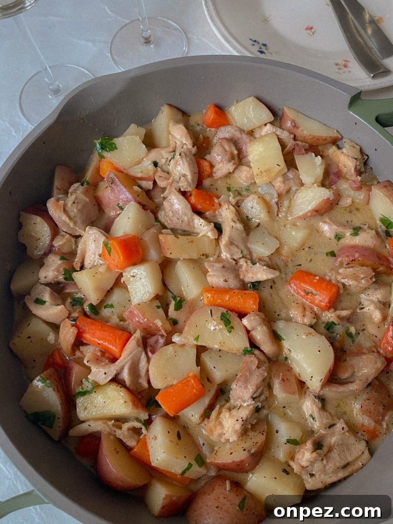 Chicken & Potatoes & Carrots in a creamy white wine sauce in a skillet with chopped carrots and herbs. 