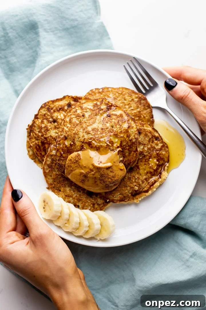 hands holding a white plate with oatmeal banana pancakes over a blue napkin.