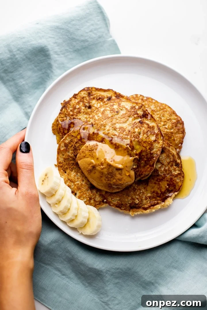 A hand holding a white plate with oatmeal banana pancakes over a blue napkin.