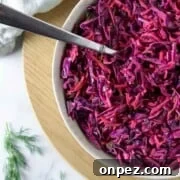 Red cabbage slaw in a bowl with a spoon on a wooden surface.