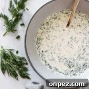 A bowl with herbed yogurt sauce next to fresh dill sprigs and a napkin.