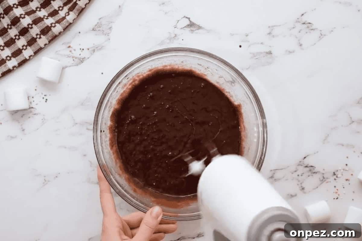 Hot Cocoa Cookies Recipe: Rich Chocolate Chip Cookies 7 beating wet ingredients for hot chocolate cookies in a glass bowl with a hand mixer.