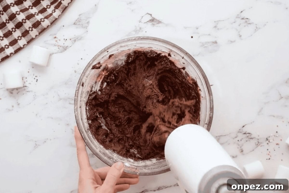 Hot Cocoa Cookies Recipe: Rich Chocolate Chip Cookies 8 beating hot chocolate cookie dough in a glass bowl with a hand mixer.