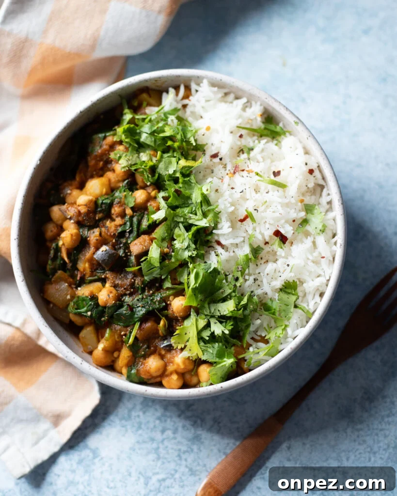 Chickpea, Eggplant and Potato Curry with Spinach Recipe 5 top view of a light blue ceramic bowl filled with vegan chickpea potato eggplant curry served with white rice and cilantro.