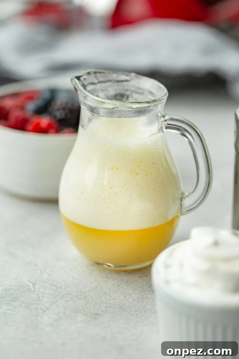 Classic Buttermilk Syrup Recipe for Pancakes and Waffles 4 a photo of a small glass pitcher of buttermilk syrup showing the large amount of foam that forms when the baking soda is first added.