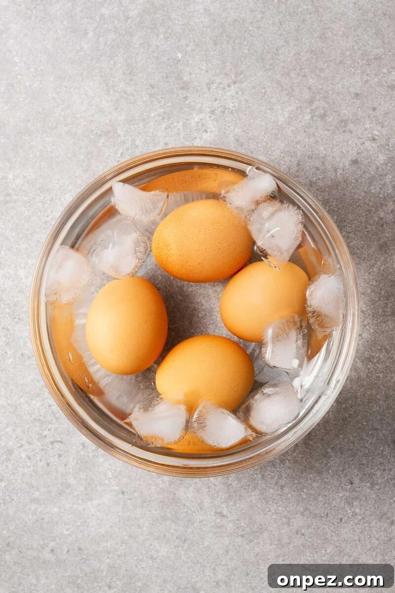 Four boiled eggs in a bowl of water with ice cubes.