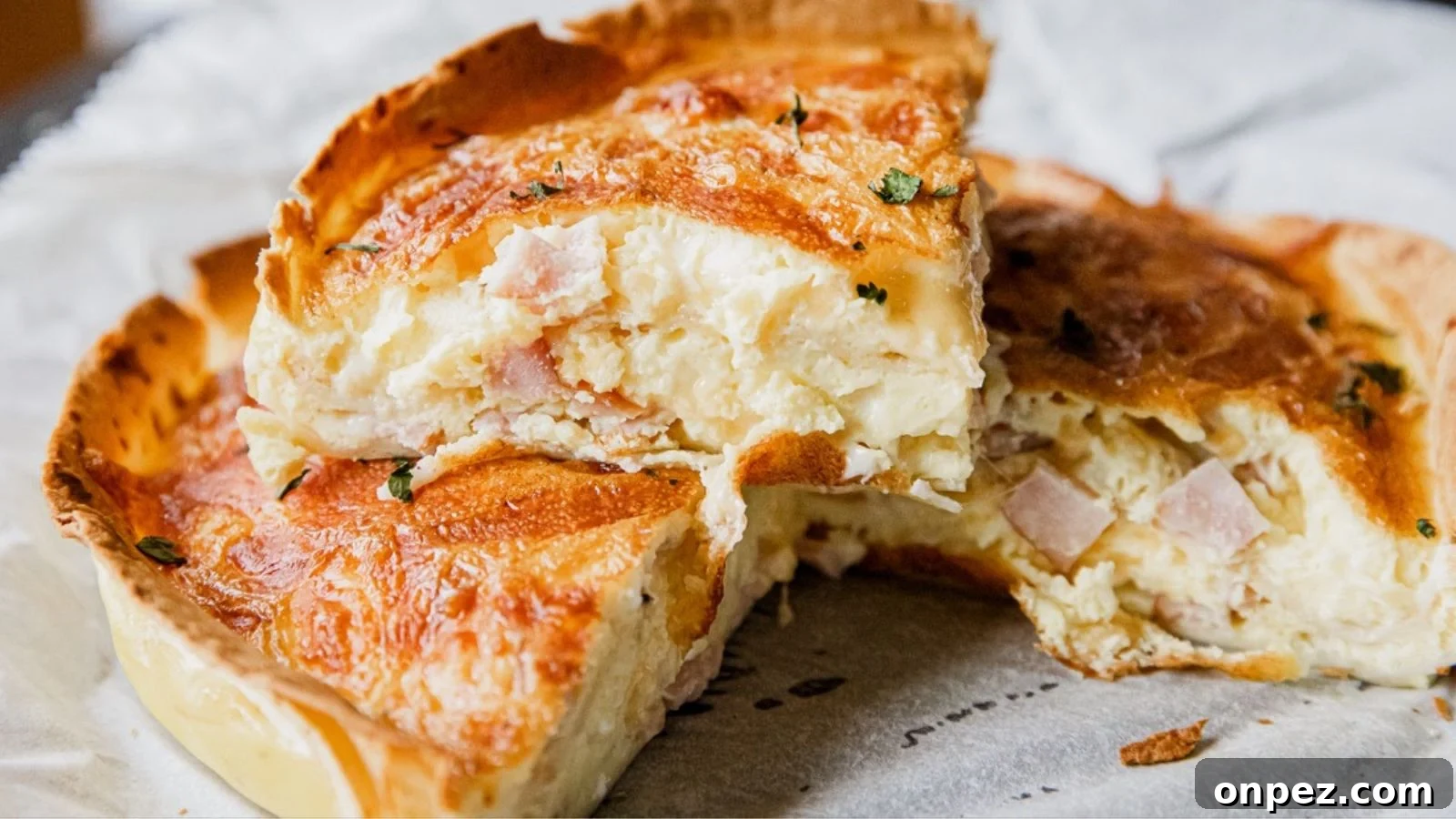 A close-up of a sliced quiche showing a golden-brown crust and a creamy filling with visible pieces of ham and herbs.