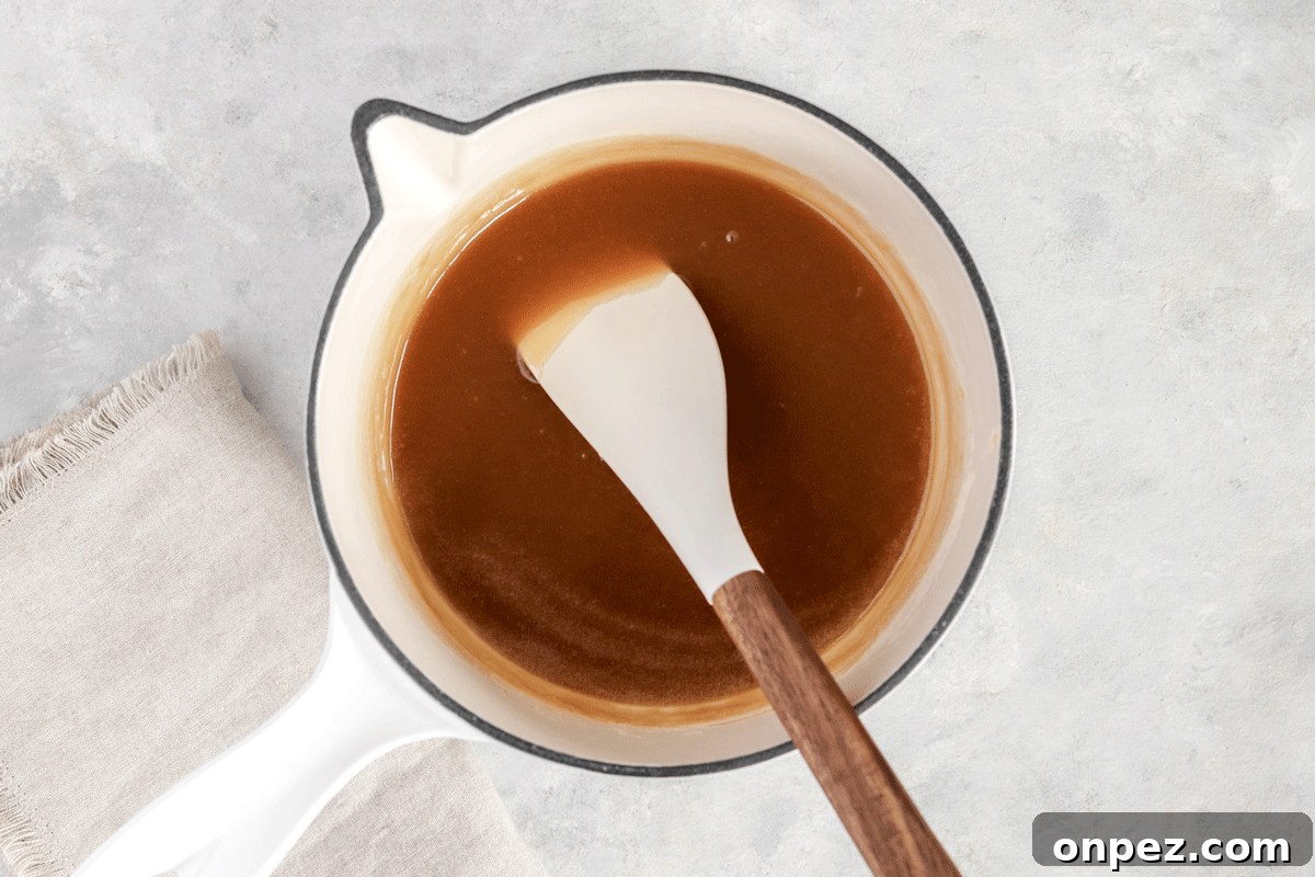 caramel sauce in a jar on a plate with apple slices on it. There is a spoon drizzling the caramel into the jar.