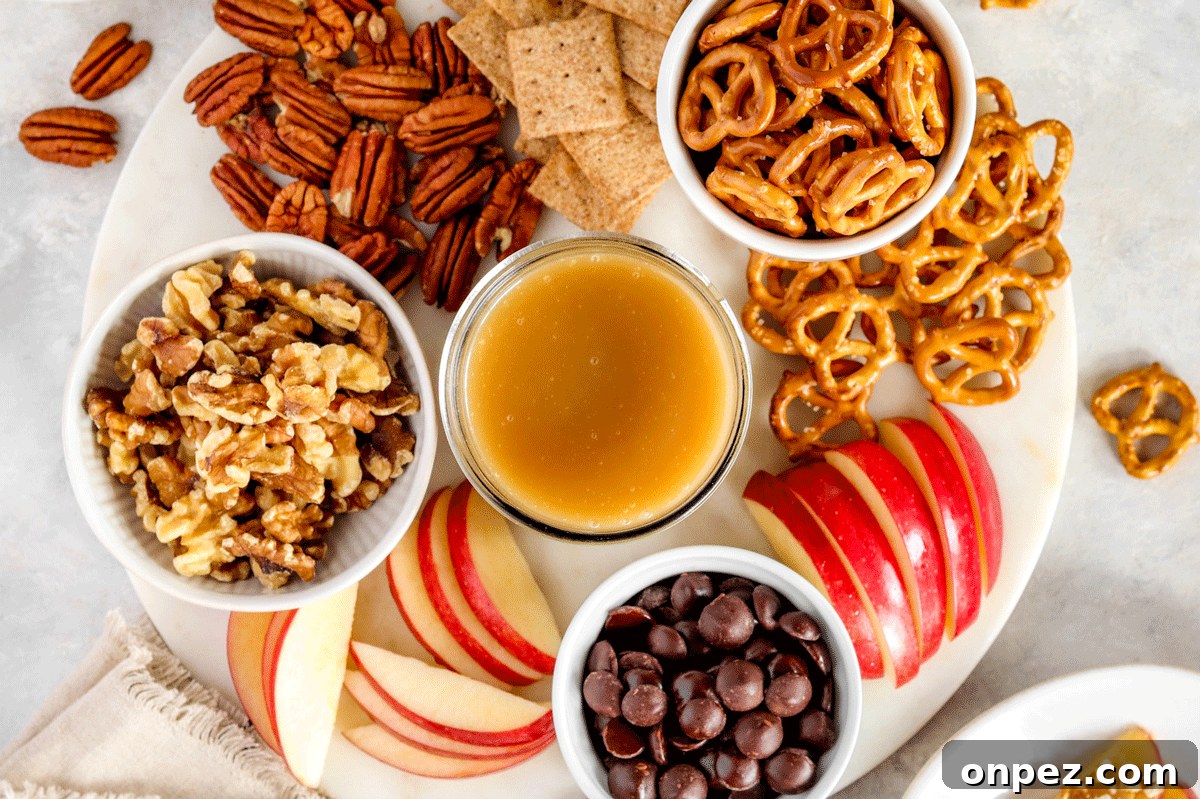 caramel dip in a jar on a charcuterie board filled with pretzels, chocolate and sliced apples. 