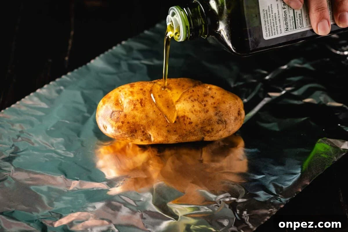How to Grill Baked Potatoes with Crispy Skin 3 A bottle of olive oil pouring onto a raw potato which is on a sheet of aluminum foil.