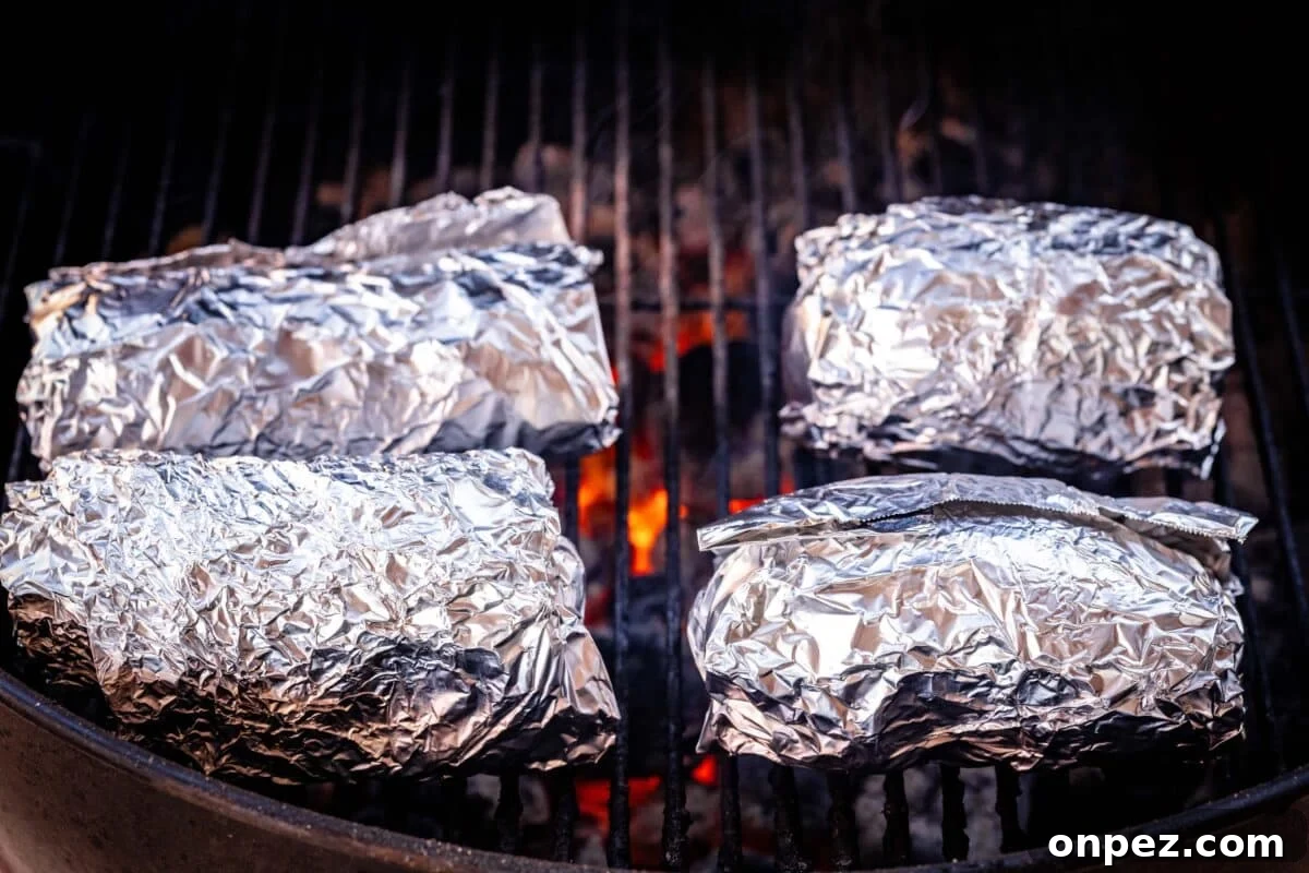 How to Grill Baked Potatoes with Crispy Skin 5 4 foil-wrapped baked potatoes on grill grates.