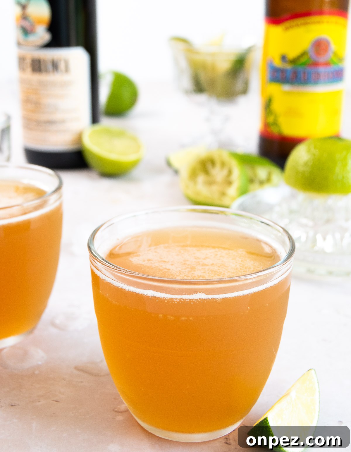 close up image of a Macunaíma cocktail in a small glass on a white surface in front of bottles and limes