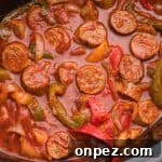 Overhead image showing sliced sausage, green, red, and yellow bell peppers, and onions simmered in red marinara sauce inside a crockpot.