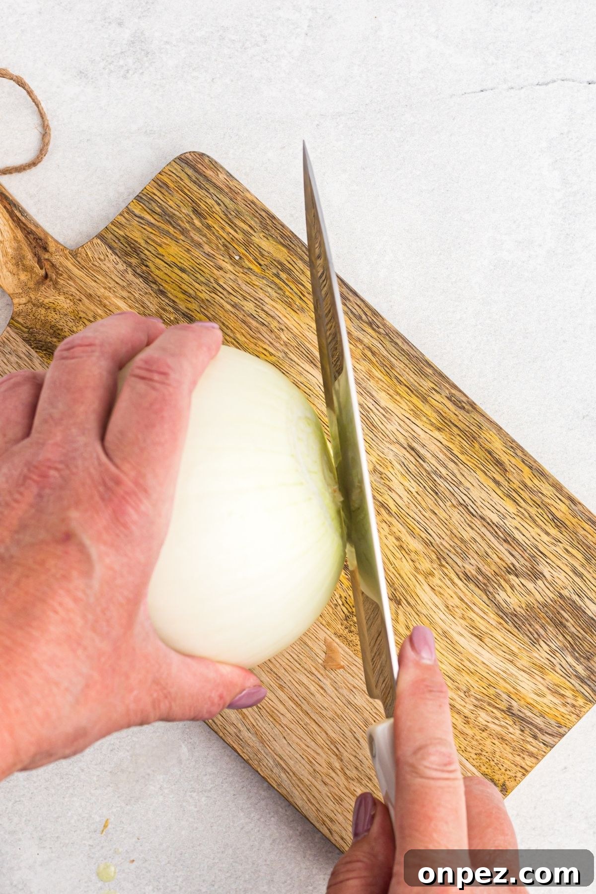 Slicing off the top of an onion on a wooden cutting board