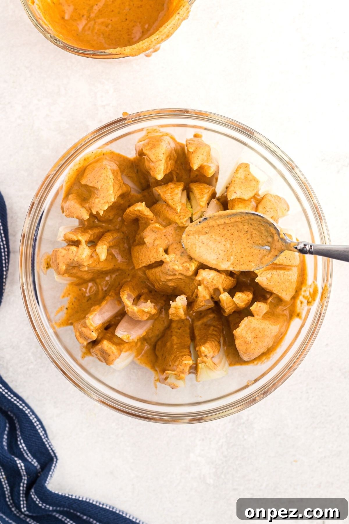 Bloomed onion in a glass bowl with a spoon drizzling batter over
