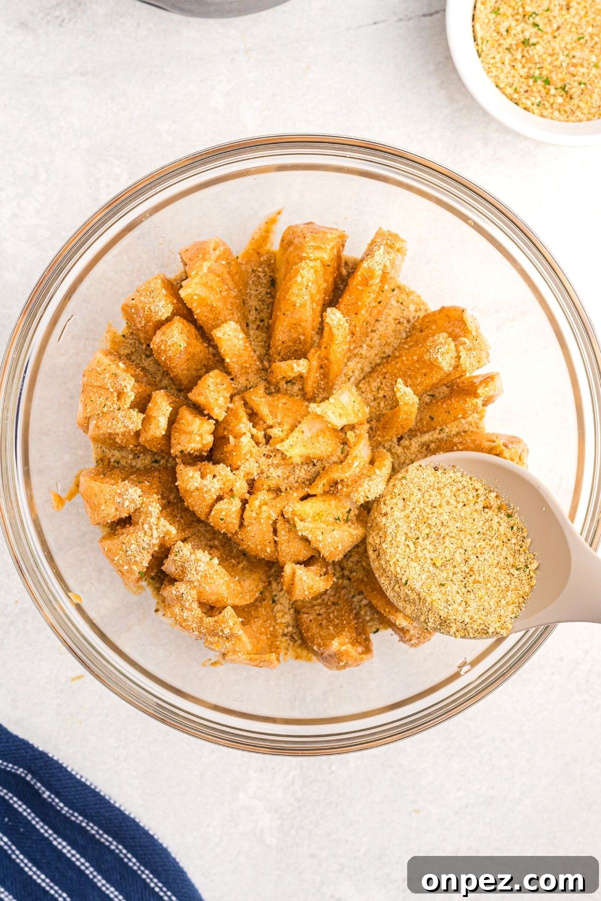 Spoon spreading breadcrumbs over battered onion in a glass bowl