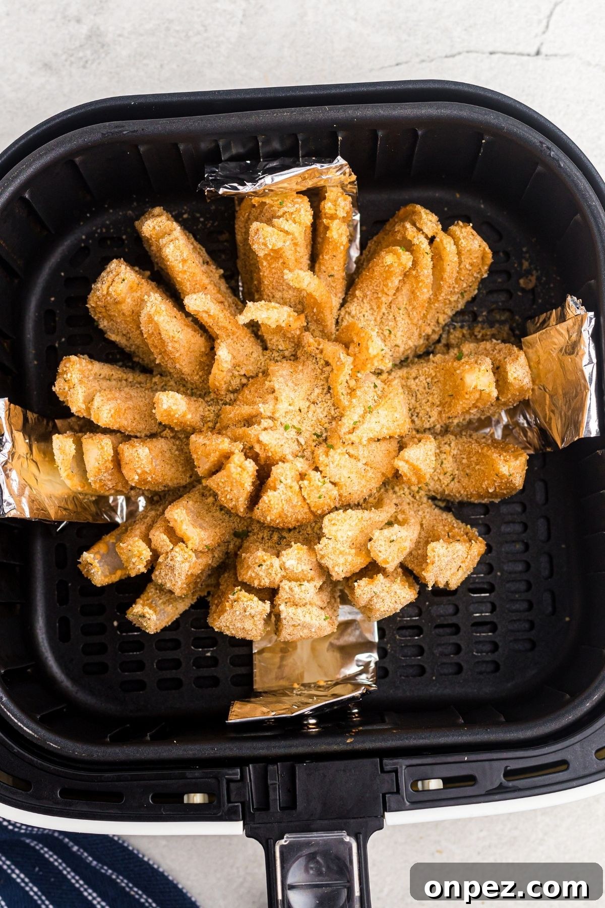 Golden battered and coated bloomed open sliced onion in the air fryer basket 