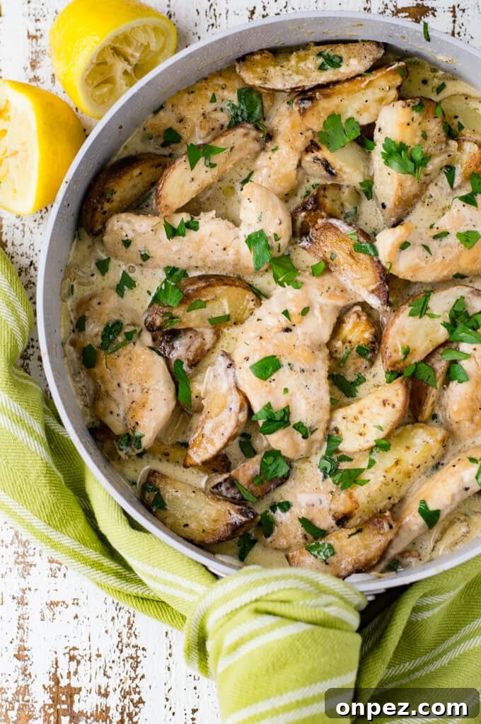 A skillet with chicken tenders and potato wedges in a lemon cream sauce with chopped parsley sprinkled on it.