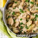 A skillet with chicken tenders and potato wedges in a lemon cream sauce with chopped parsley sprinkled on it.