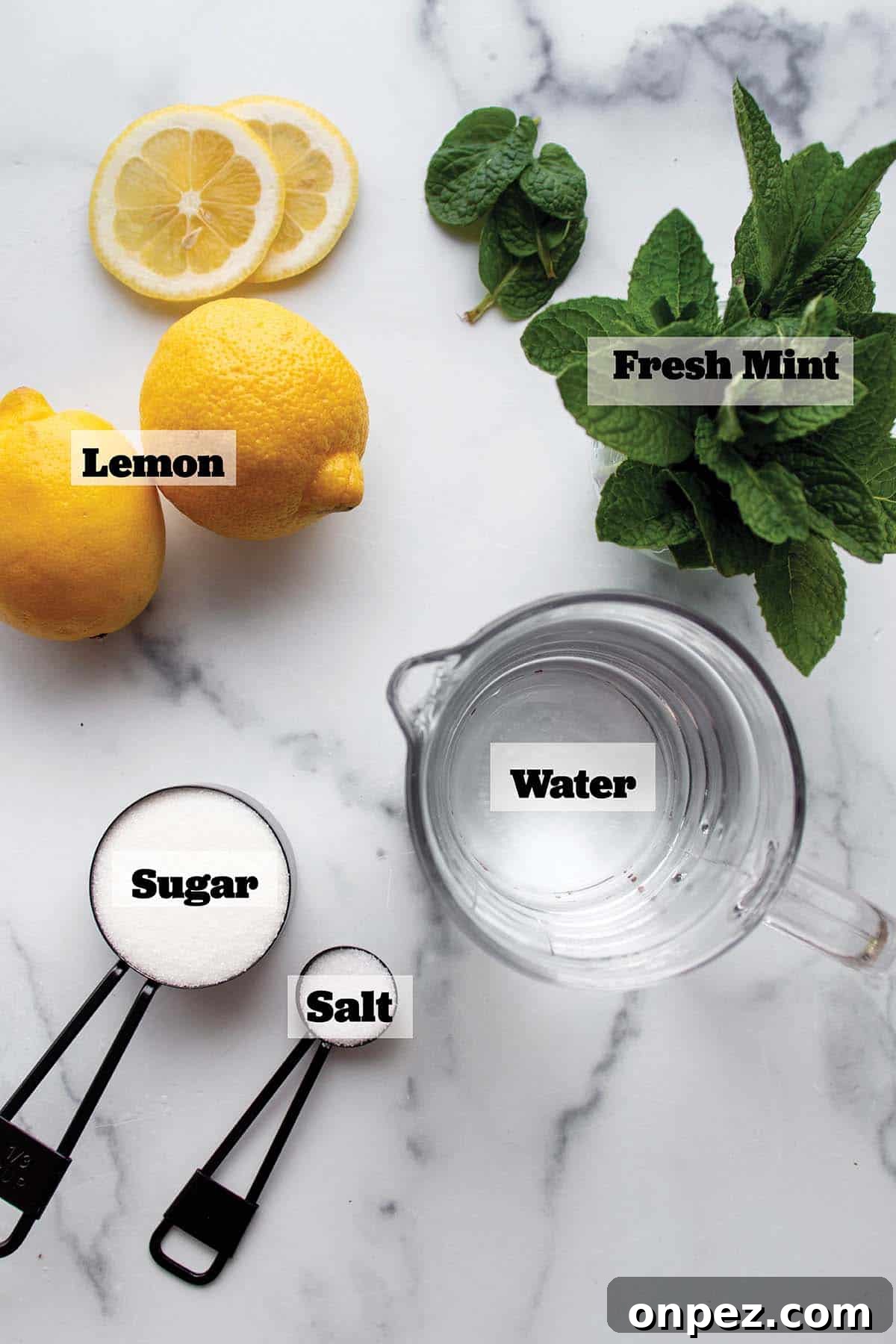 Fresh lemon, mint, a cup of water and measuring spoons with sugar and salt.