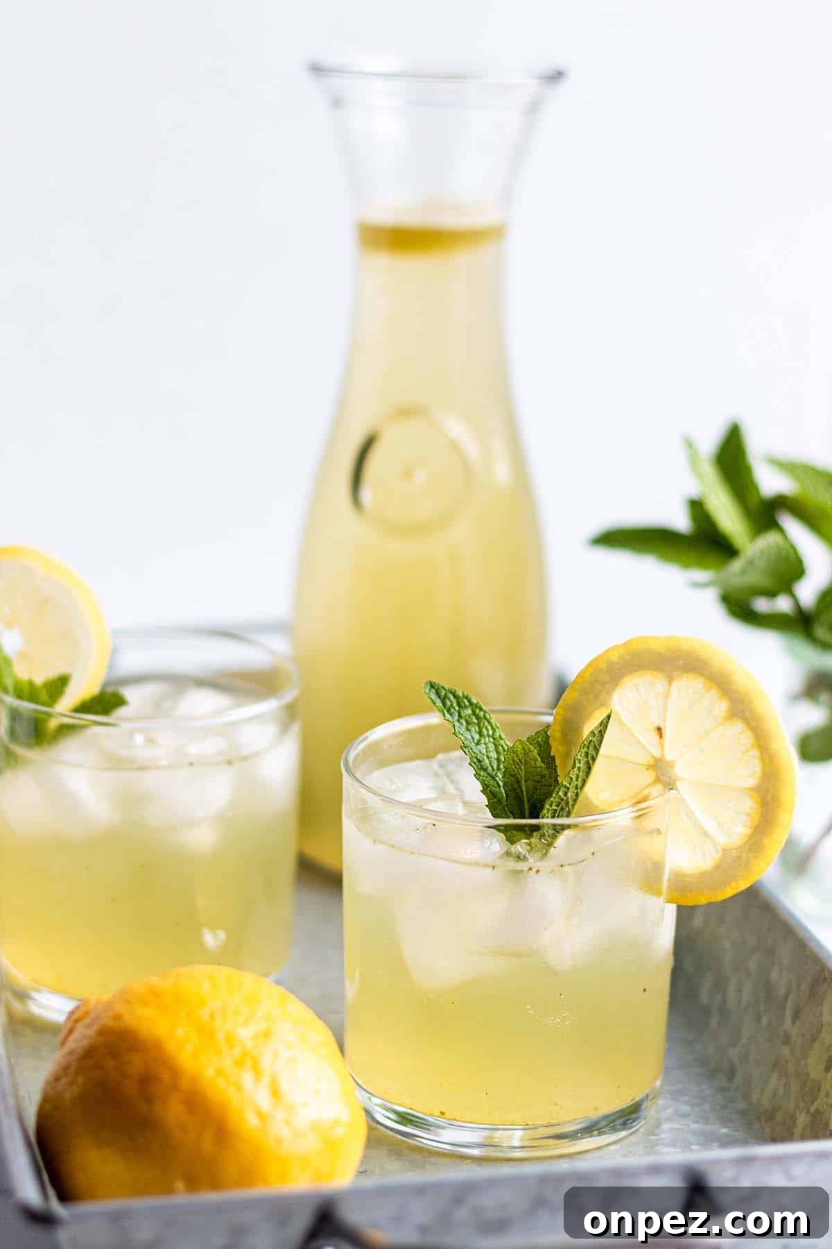 A tray with a pitcher and two glasses full of lemonade with fresh mint and lemons.