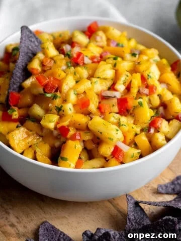 A bowl with diced mangos, pineapples and blue corn tortilla chips on a wooden board.