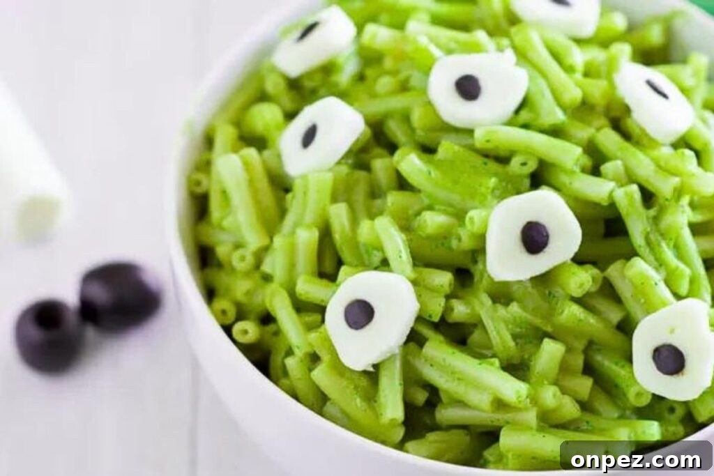 A bowl of green mac and cheese with cheese and olive eyes.